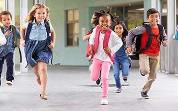 6 kids running in the school hallway wearing schoolbags