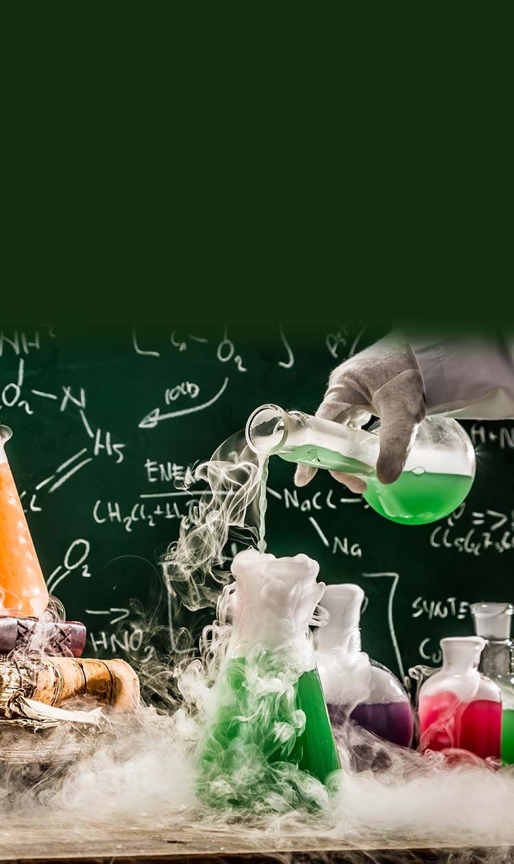 Hand pouring liquid into beaker on a desk.  Another beaker on a stack of books with smoke surrounding all beakers and table