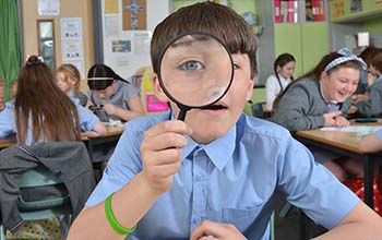 Boy in classroom looking through a magnifying glass