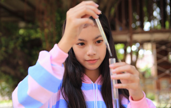 A girl in pink and blue striped sweatshirt holding a test tube with purple liquid inside.